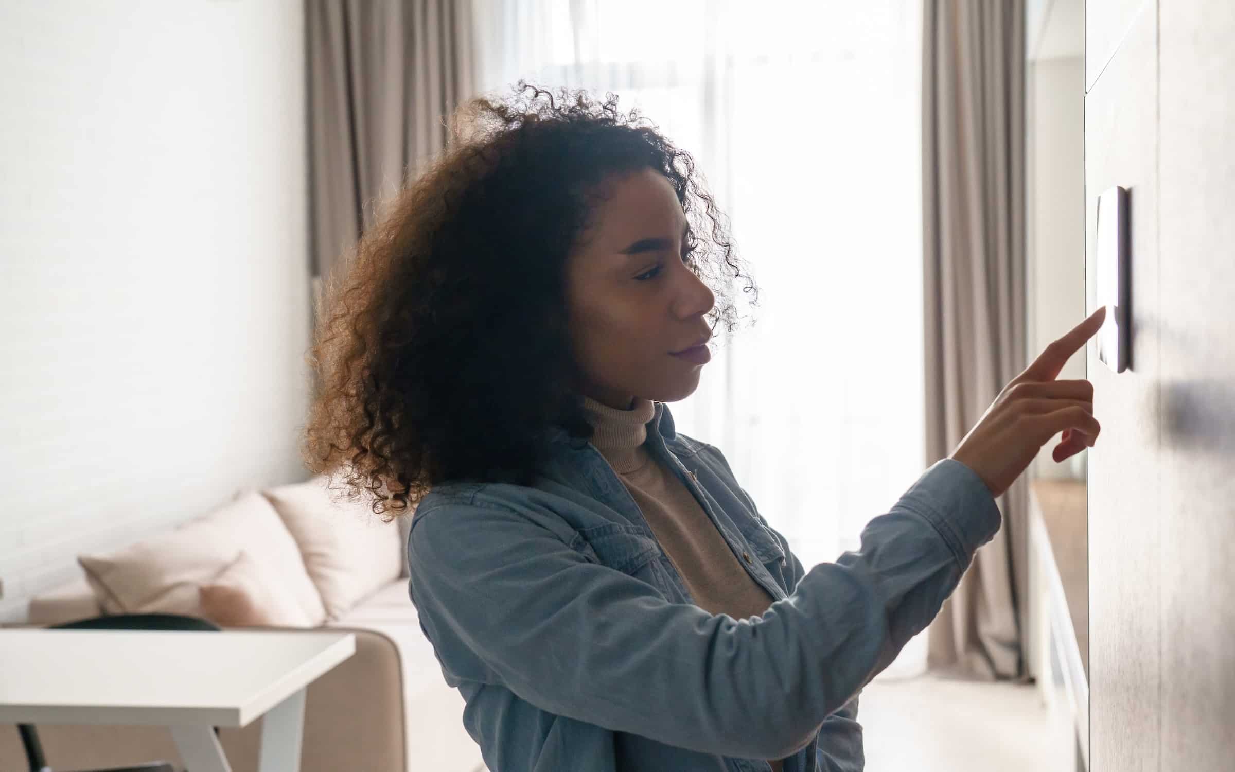 Woman using smart electric thermostat for home temperature